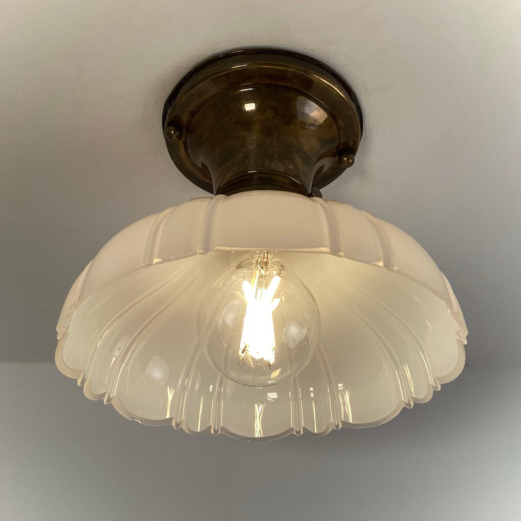 Antique brass flush mount ceiling light with scalloped milk glass shade illuminated