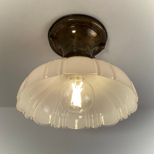 Antique brass flush mount ceiling light with scalloped milk glass shade illuminated