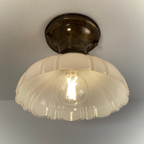 Antique brass flush mount ceiling light with scalloped milk glass shade illuminated