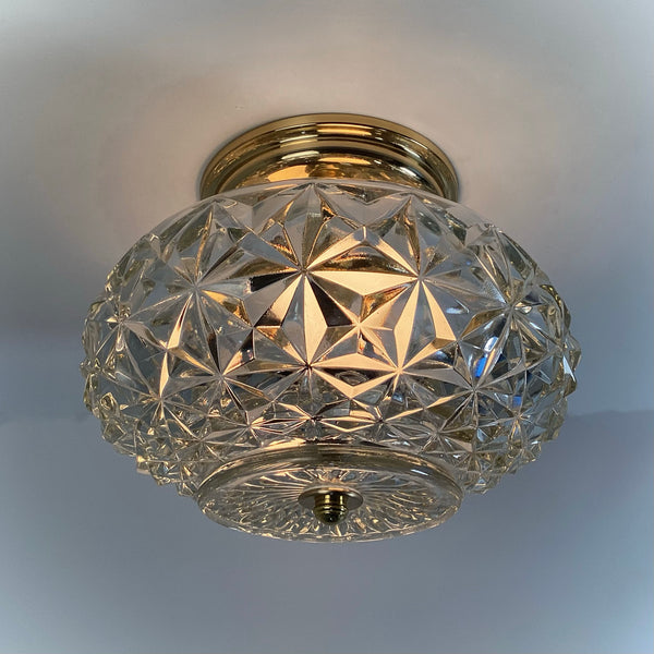 Mid-century crystal flush mount ceiling light fixture with diamond starburst glass shade and polished brass canopy, illuminated and photographed against a white ceiling — Vintporium.