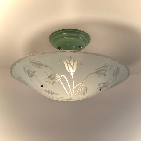 Close-up of a vintage semi-flush mount ceiling light with a mint green base and frosted glass tulip shade, illuminated.