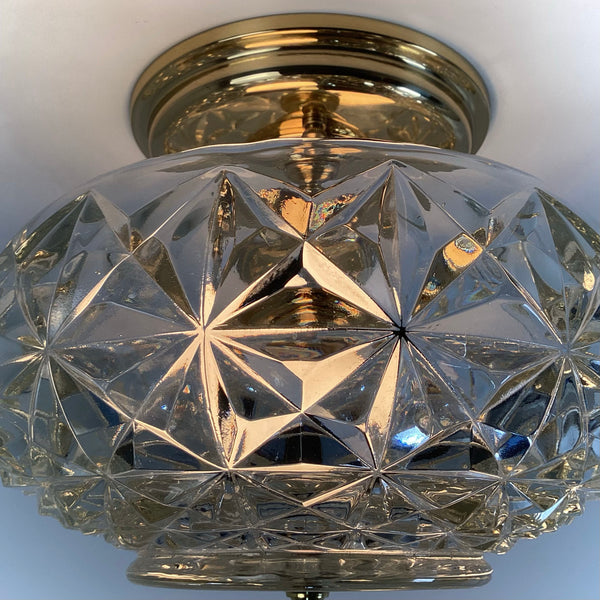 Close-up of an illuminated mid-century crystal flush mount ceiling light showcasing the faceted diamond starburst glass pattern and polished brass canopy reflecting warm light — Vintporium.