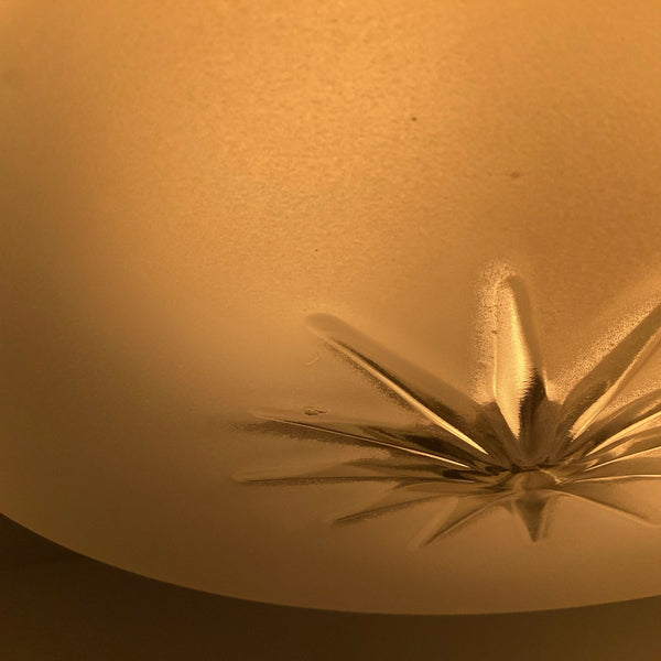 Close-up of 1950s frosted glass ceiling shade showing embossed starburst design illuminated with a warm glow.