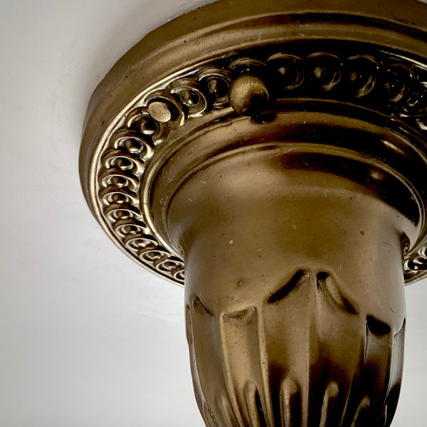 Close-up of the antique brass ceiling canopy on a 1920s pendant light, showing the embossed beaded rim and fluted column detail