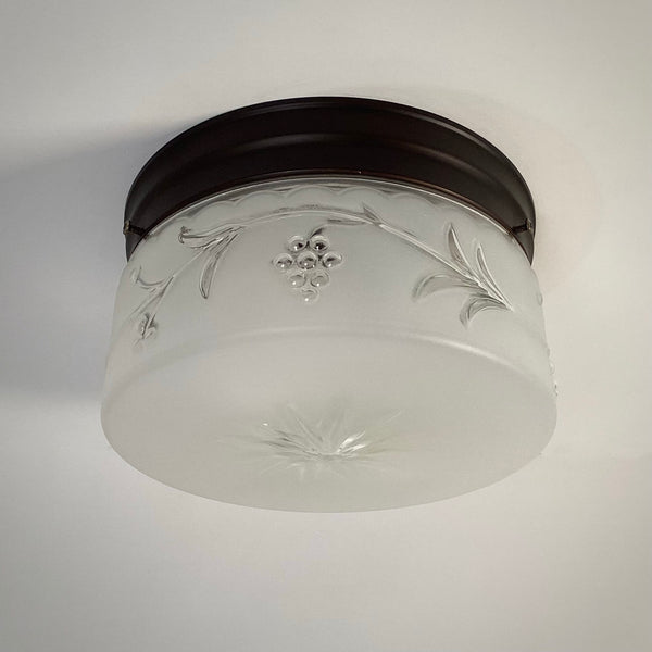 Vintage frosted glass ceiling fixture from the 1940s with raised grapevine motif and starburst bottom, shown unlit.