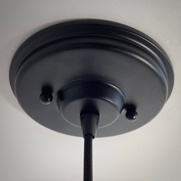 A matte black metal ceiling canopy successfully mounted flush against a white ceiling, featuring a black cord grip and two matching decorative screw caps.