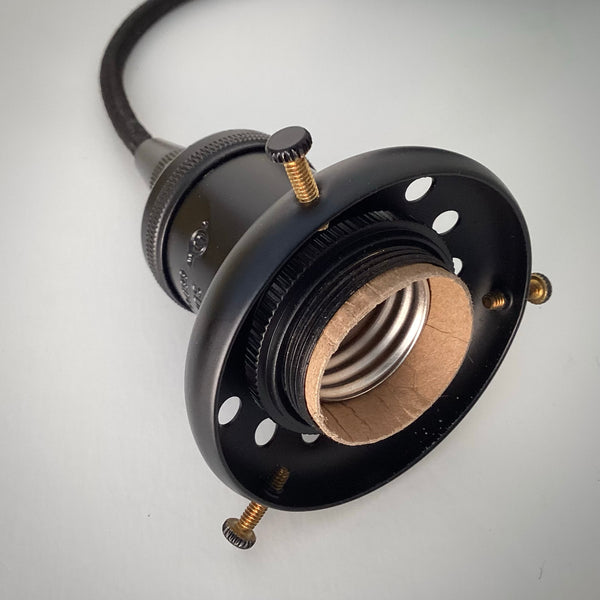 A close-up of a black E26 light bulb socket featuring an attached 2.25-inch shade fitter with three brass thumb screws for securing a glass lamp shade.