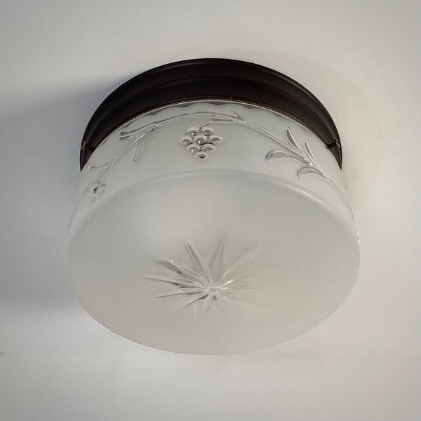 Unlit mid-century flush-mount ceiling light with embossed frosted glass shade featuring grape cluster and starburst motif.