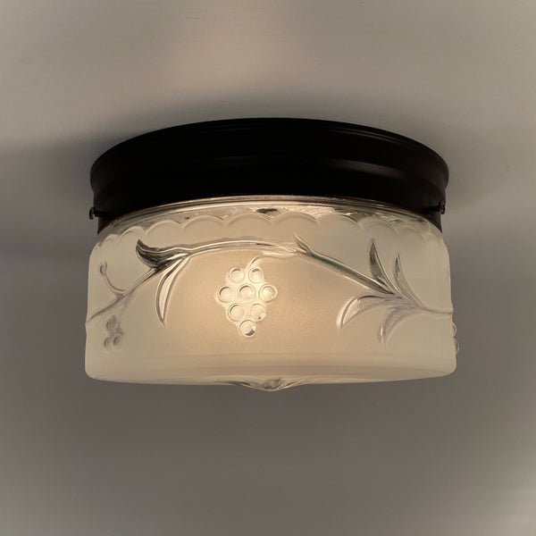 Close-up of illuminated frosted glass ceiling shade with raised grapevine and leaf detailing from the 1940s.