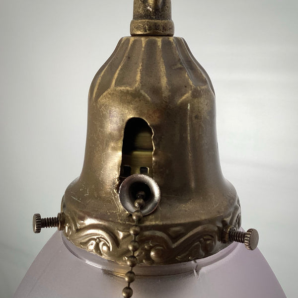 Close-up of the antique brass shade holder on a 1920s pendant light, showing the pull-chain socket opening, patina, and cloth-wrapped cord.