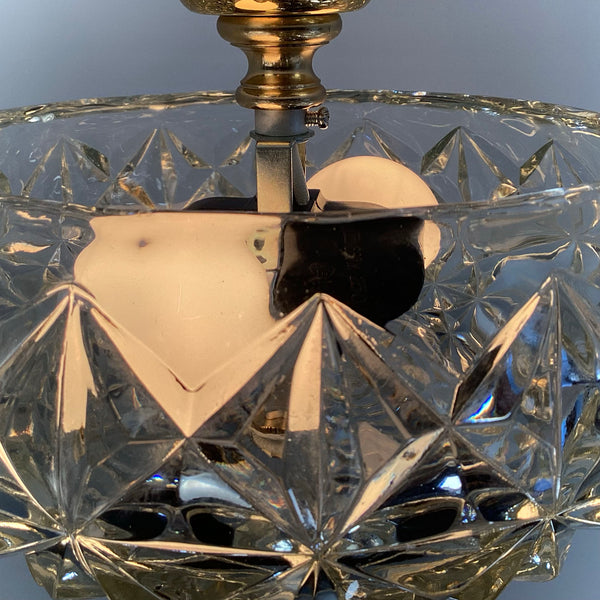 Close-up view of the interior of a mid-century crystal flush mount ceiling light showing dual sockets and diamond starburst patterned glass shade with brass hardware — Vintporium.