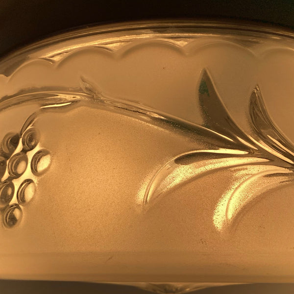 Detailed illuminated view of mid-century frosted glass ceiling shade showing embossed grape cluster and vine pattern.